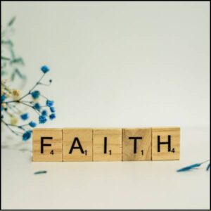A wooden block that says 'faith' next to blue flowers